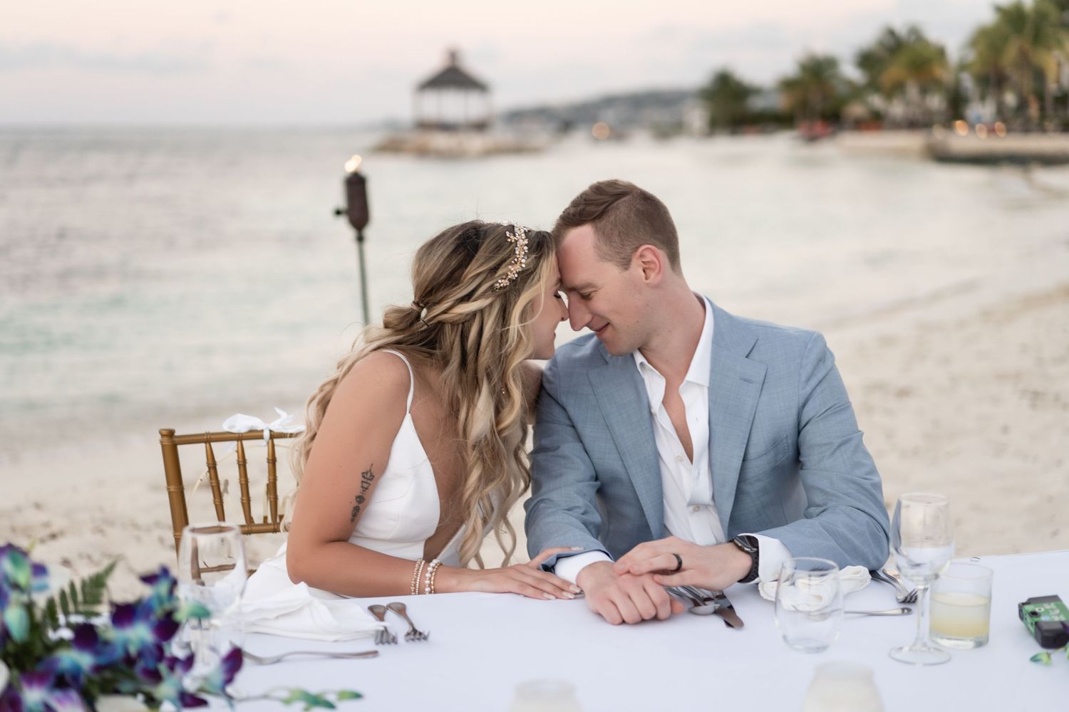 Couple sitting at decorated beach reception table sharing intimate moment.