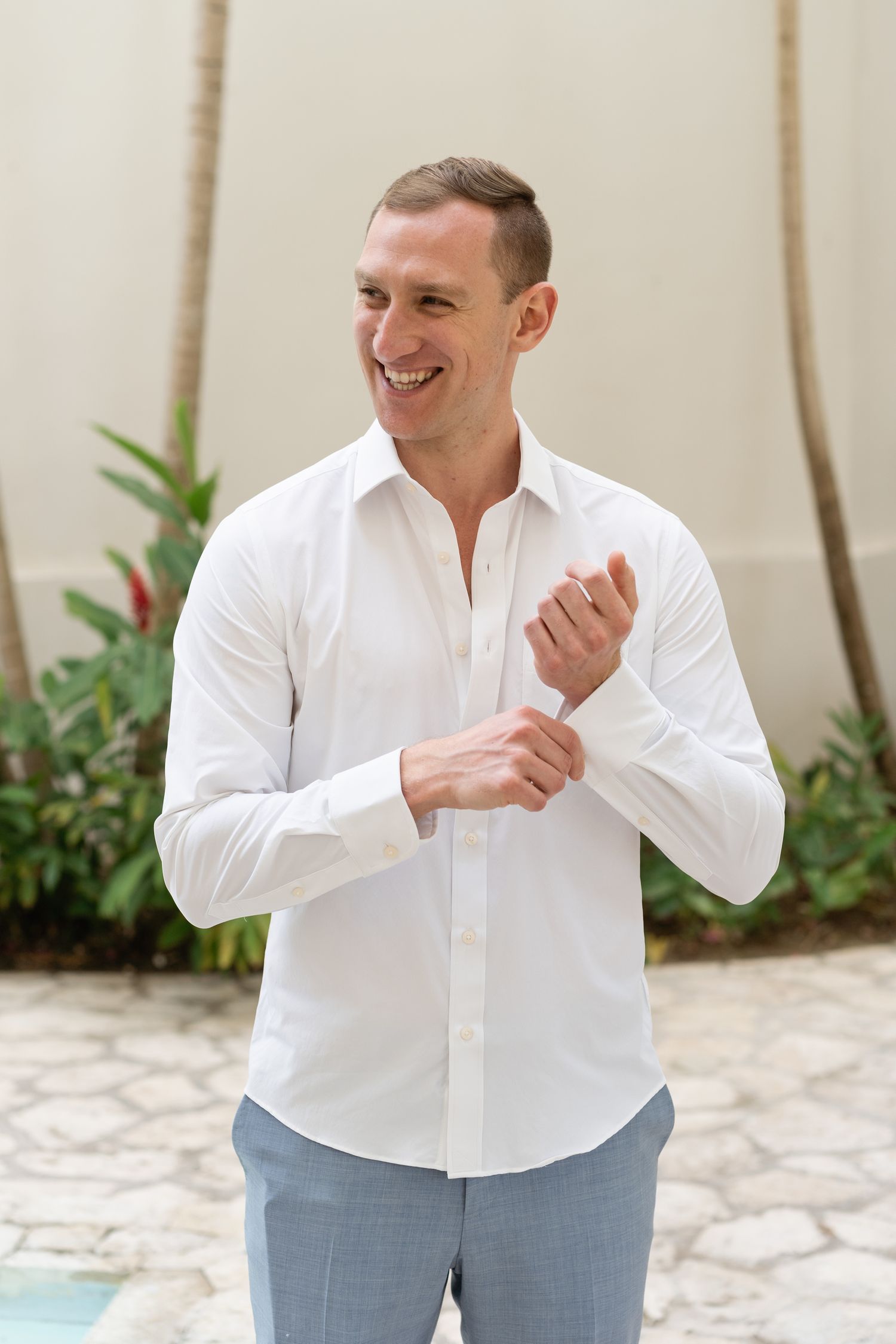 A groom in a crisp white shirt adjusts his cuffs while smiling.