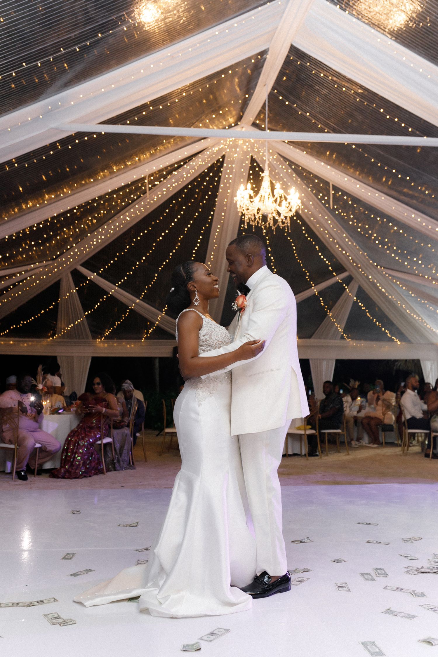 Romantic first dance under crystal chandelier and twinkling lights in wedding tent.