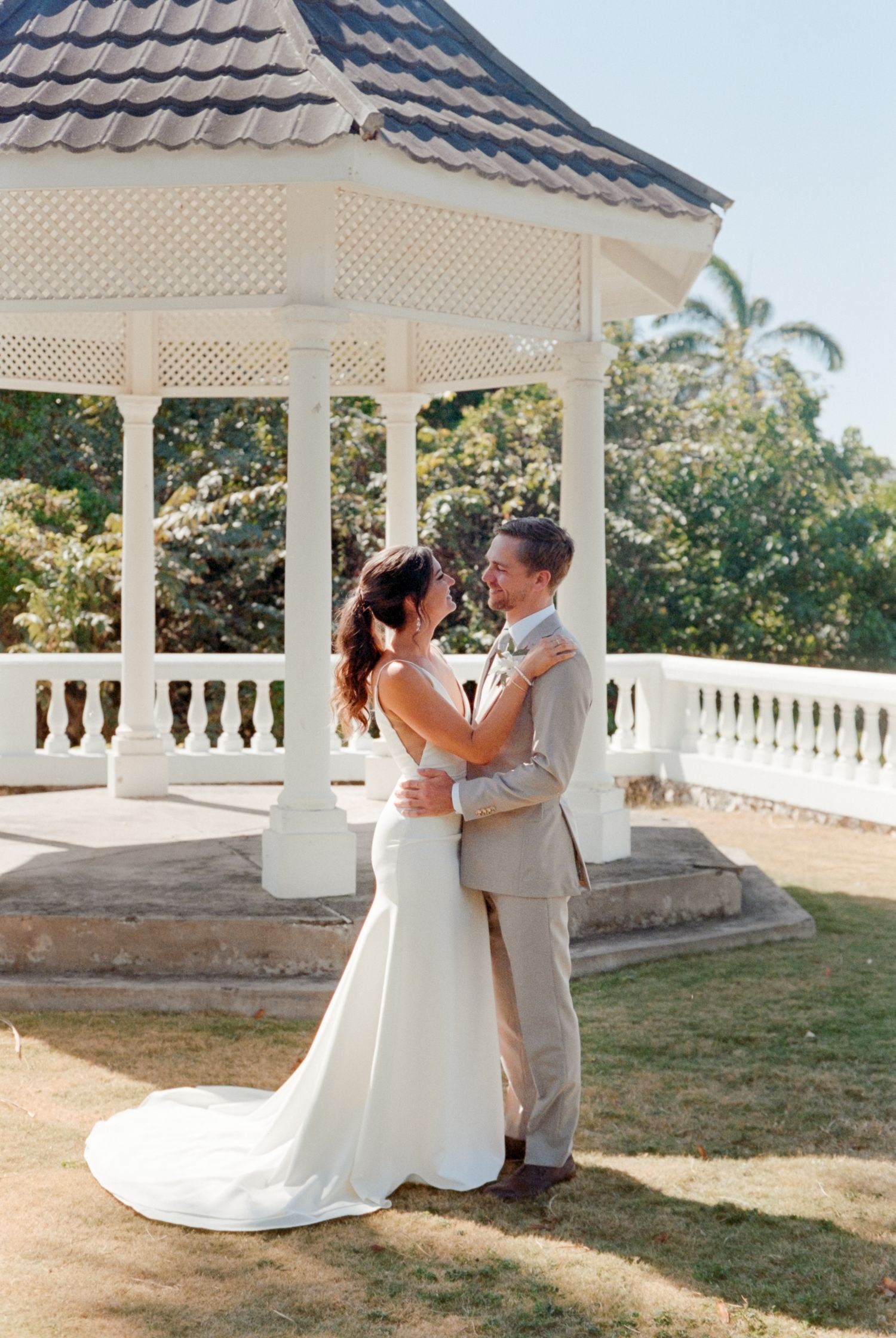 A romantic wedding moment captured under a white gazebo surrounded by tropical landscaping.