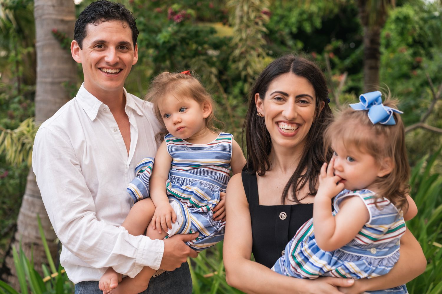Family portrait in tropical garden setting with palm trees and coordinated casual attire.