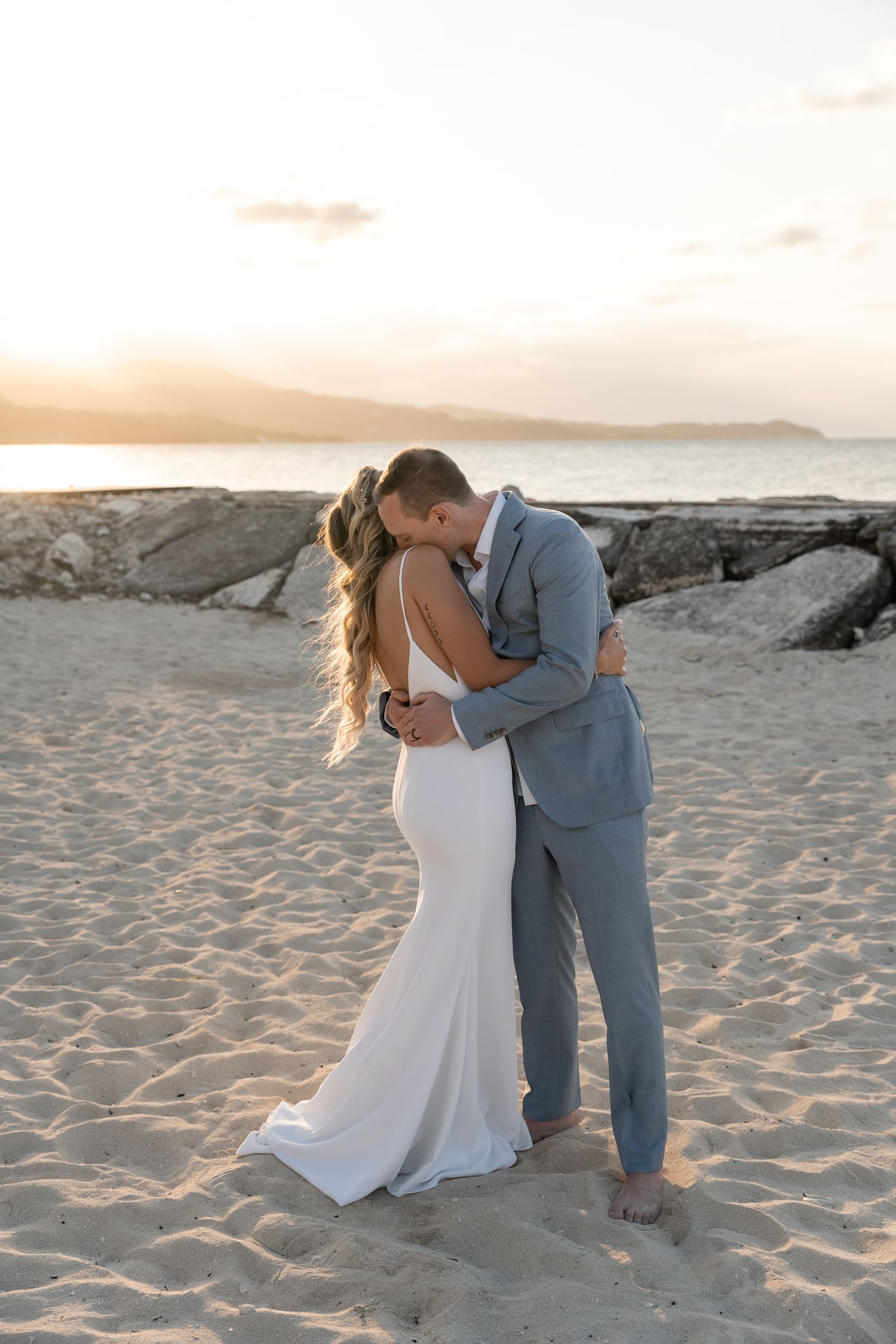 A romantic embrace on a sandy beach at sunset with ocean views.