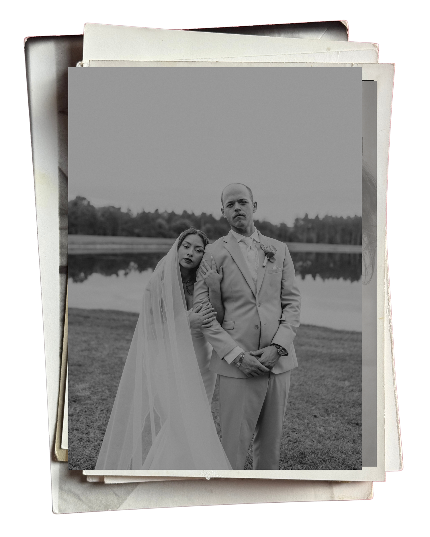 Black and white wedding photo of bride in veil and groom in suit standing by a lake surrounded by trees.