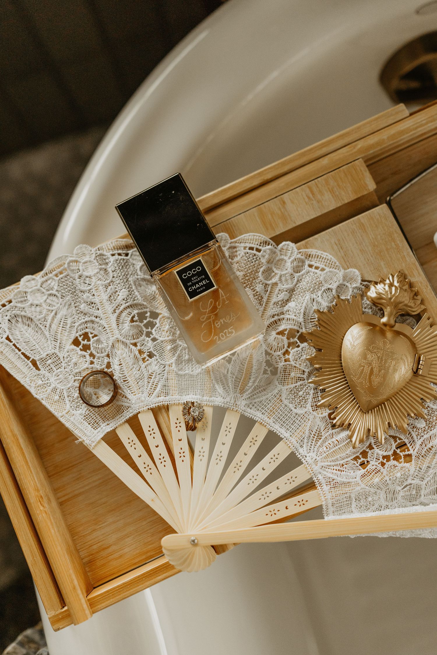 Elegant white lace fan displayed with perfume bottle and gold heart pendant on wooden surface.