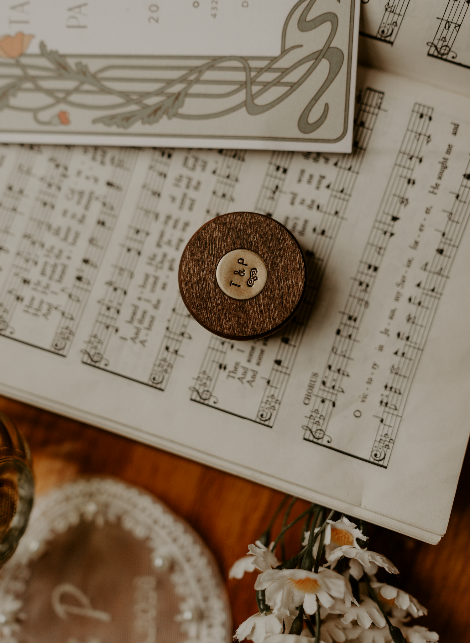 Wooden circular music box resting on vintage sheet music with white daisies and decorative elements nearby.