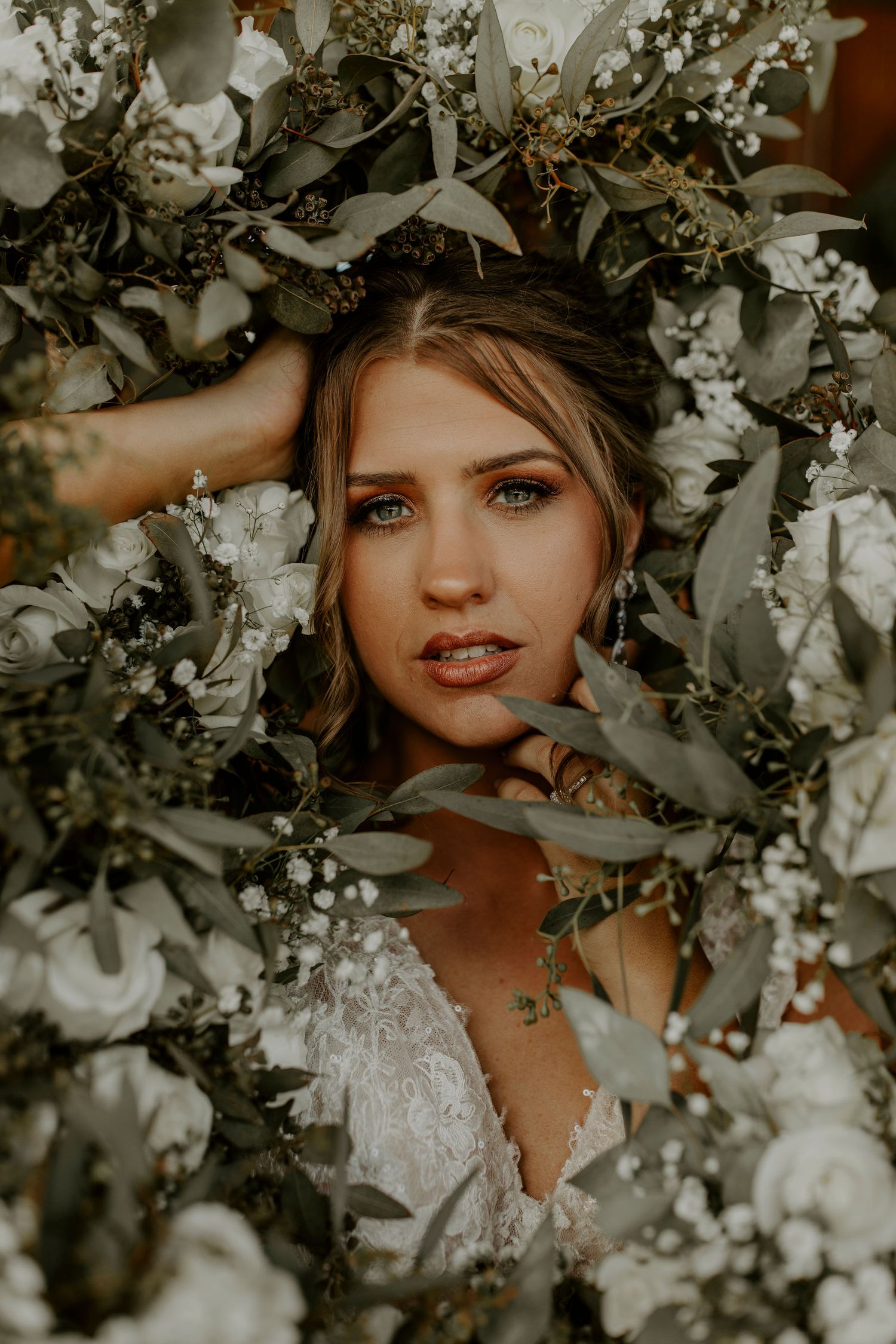 Artistic wedding portrait framed by white flowers and greenery with moody warm tones and natural lighting.