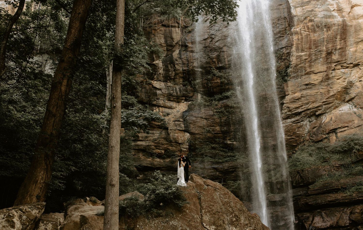 A thin waterfall cascading down a rocky cliff face in a scenic wilderness landscape.