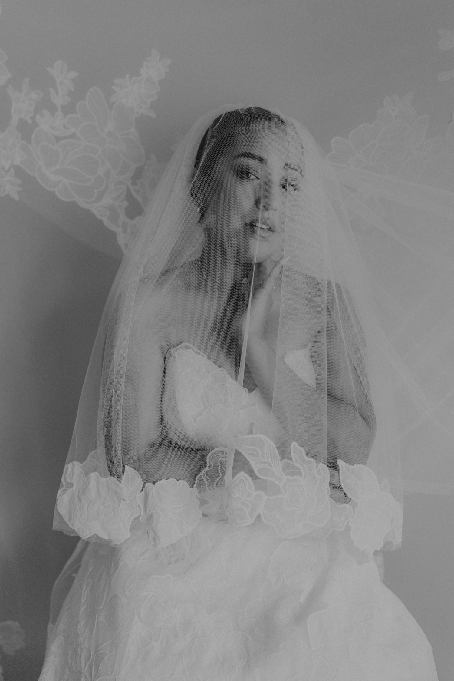Black and white bridal portrait of a woman in a strapless gown and floral-trimmed veil.