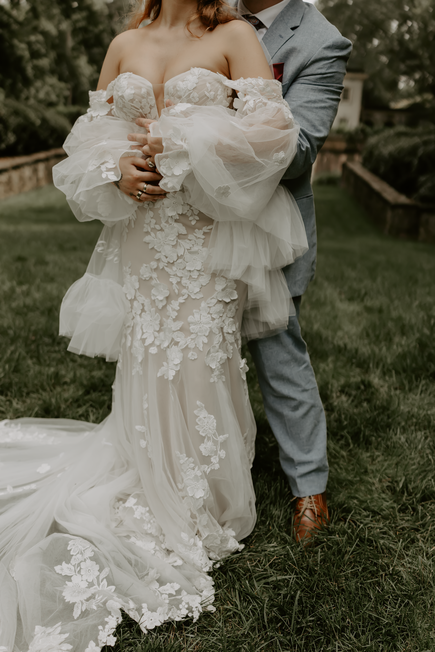 Close-up details of a romantic wedding dress with delicate floral appliques and flowing tulle fabric in an outdoor setting.