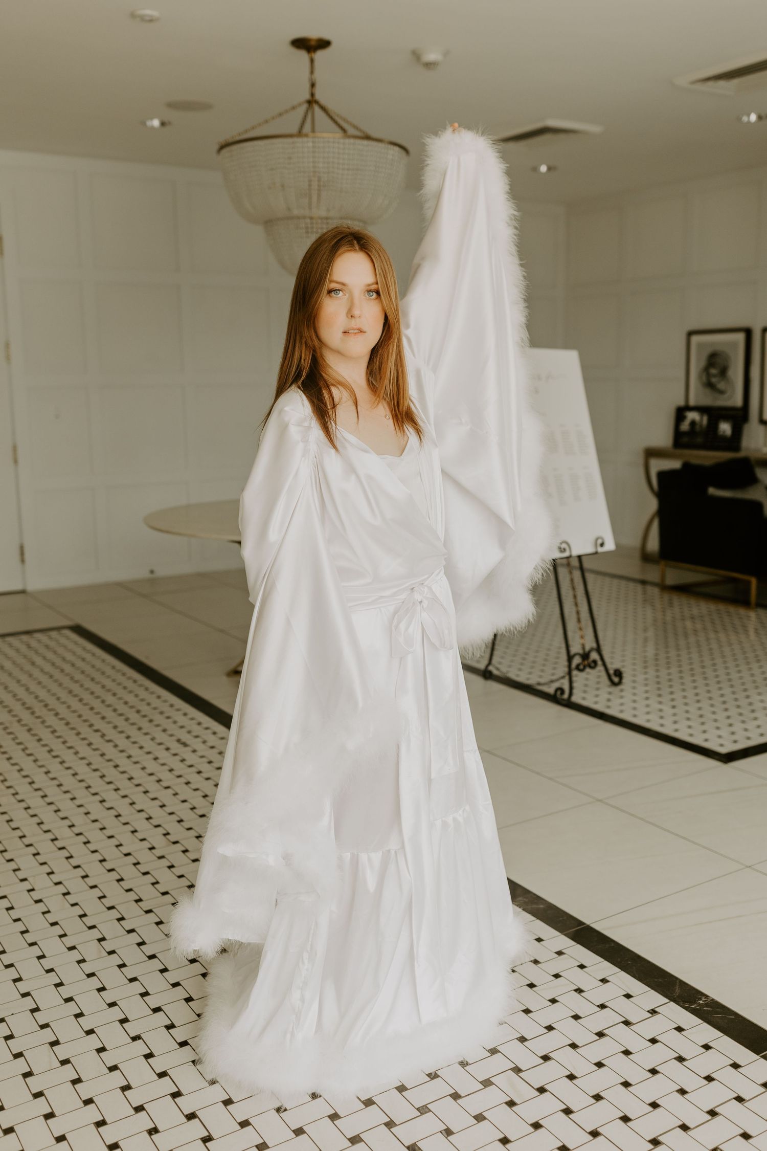 A flowing white wedding dress with long sleeves is displayed in an elegant room with black and white tiled flooring.