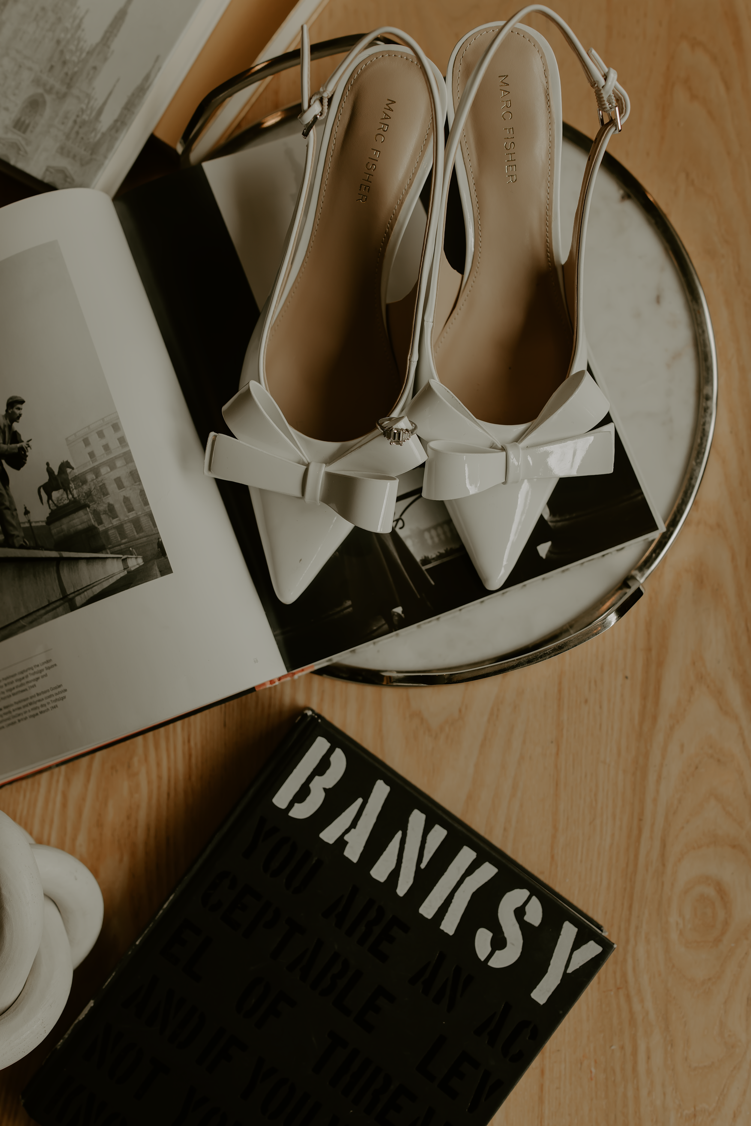 White pointed-toe high heel shoes arranged with black and white fashion magazine pages on a wooden surface.