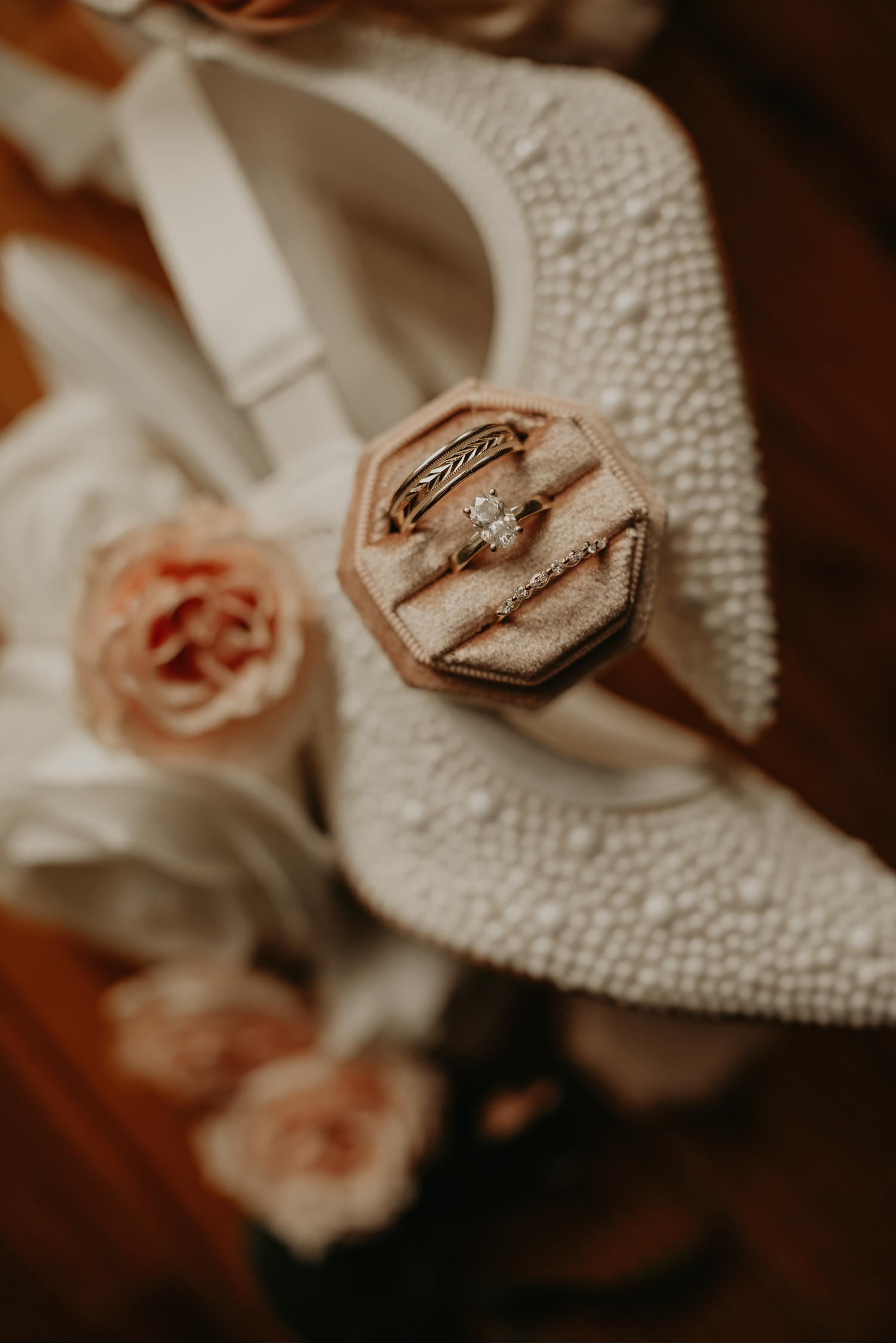 Wedding rings nestled on textured white shoe with pink roses.