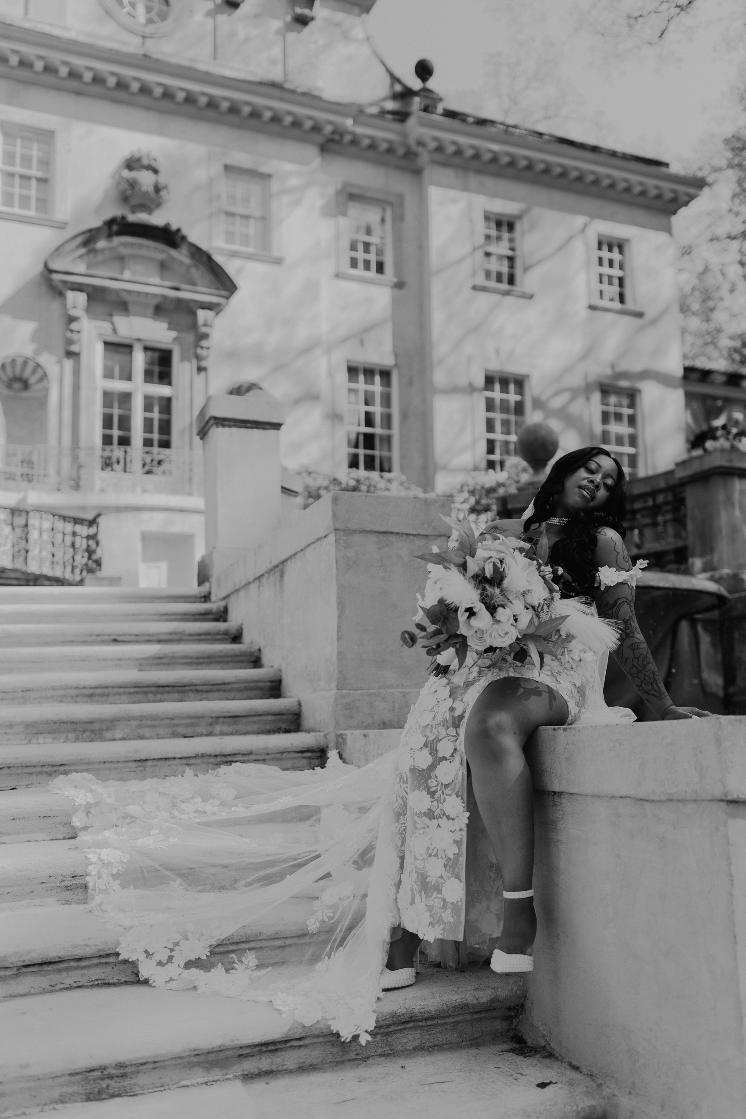 Black and white photo of an elegant wedding dress with flowing train on marble steps of a grand historic mansion.