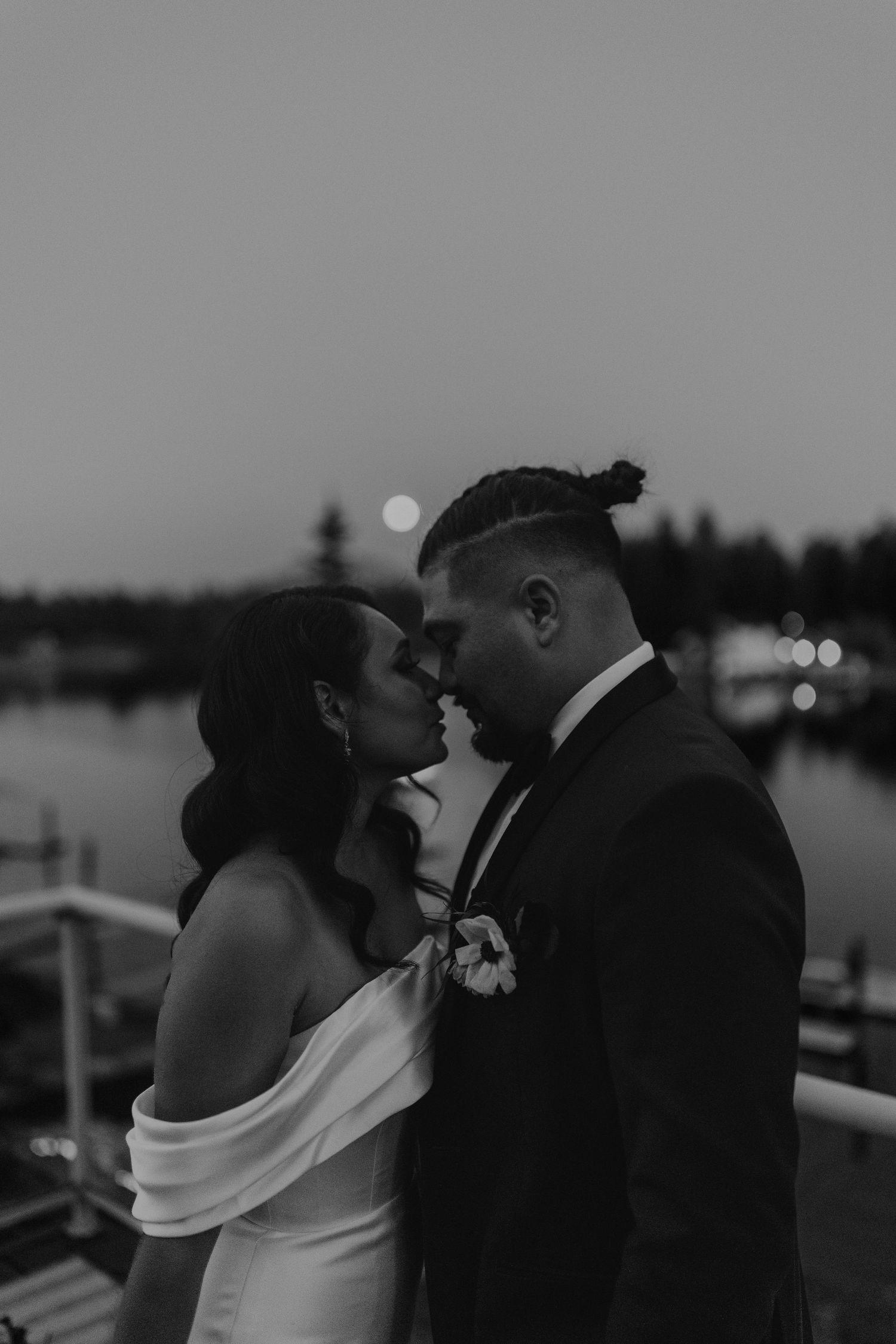 Black and white wedding photo series showing romantic couple embracing at sunset by a waterfront.