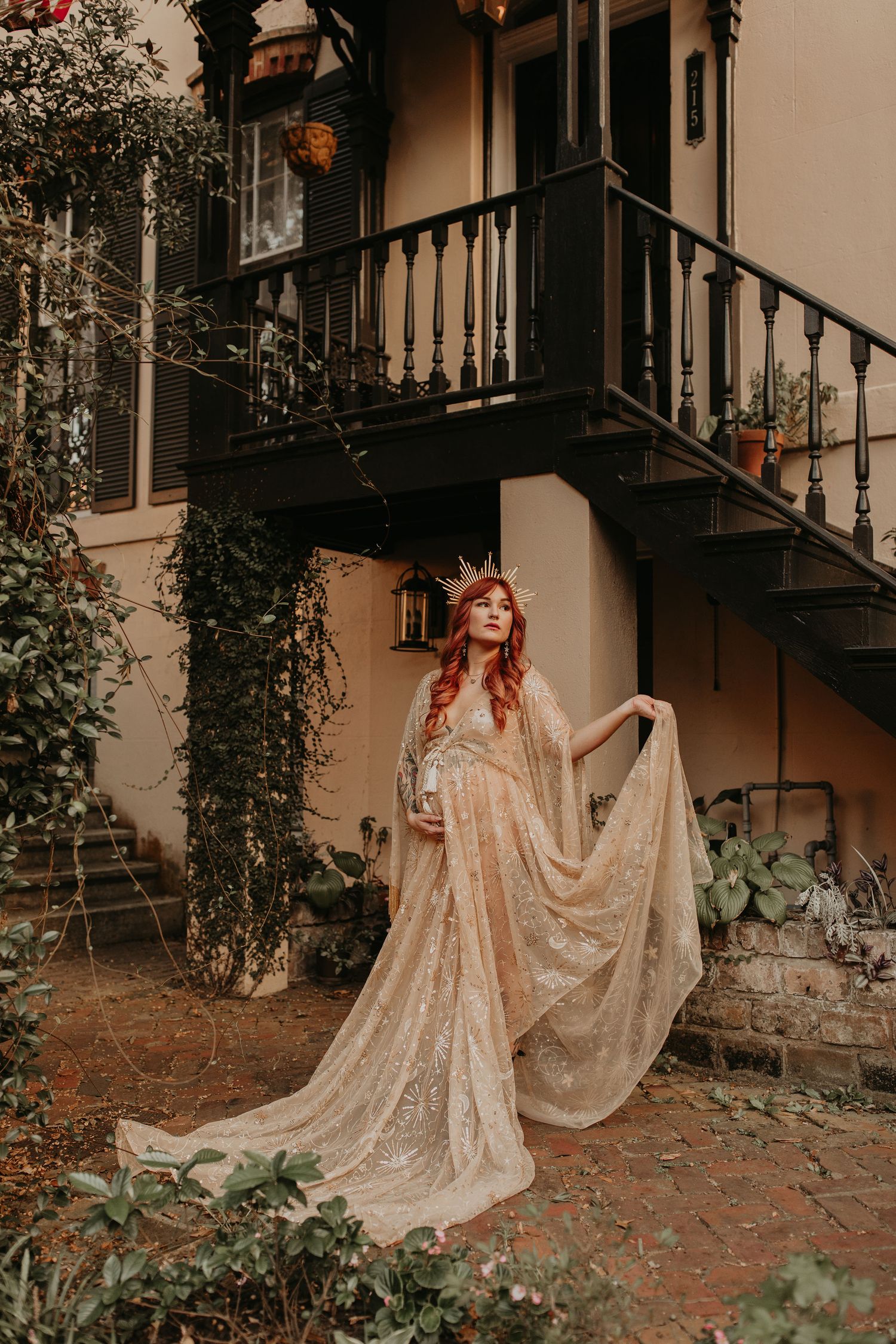 A vintage-style portrait in a romantic garden setting with a flowing lace dress against a historic building exterior.