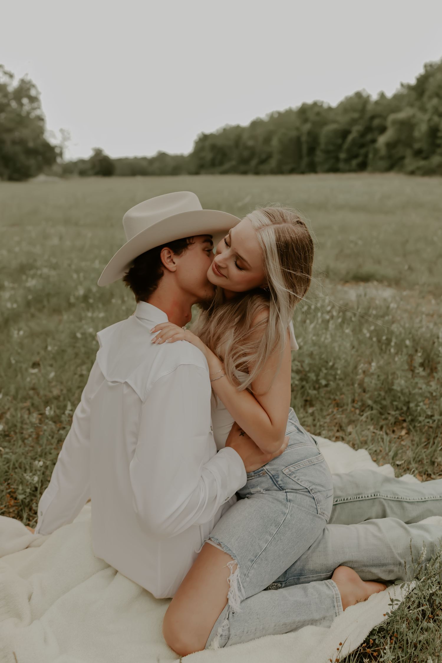 Romantic couple in casual wear sharing an intimate moment on a blanket in a meadow.