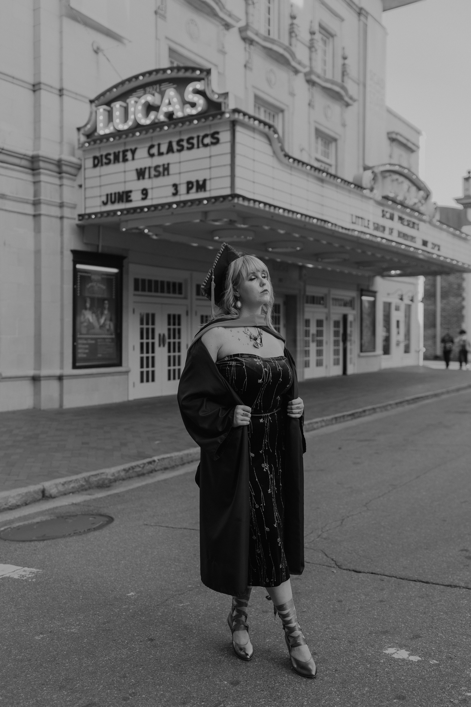 A person in a black dress poses in front of the historic Lucas Theatre marquee showing Disney Classics on a cloudy day.