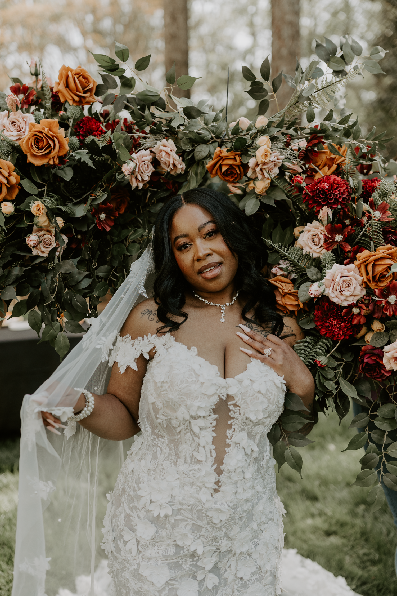 Beautiful bridal portrait with lush floral arrangement featuring orange roses and greenery in a romantic outdoor setting.