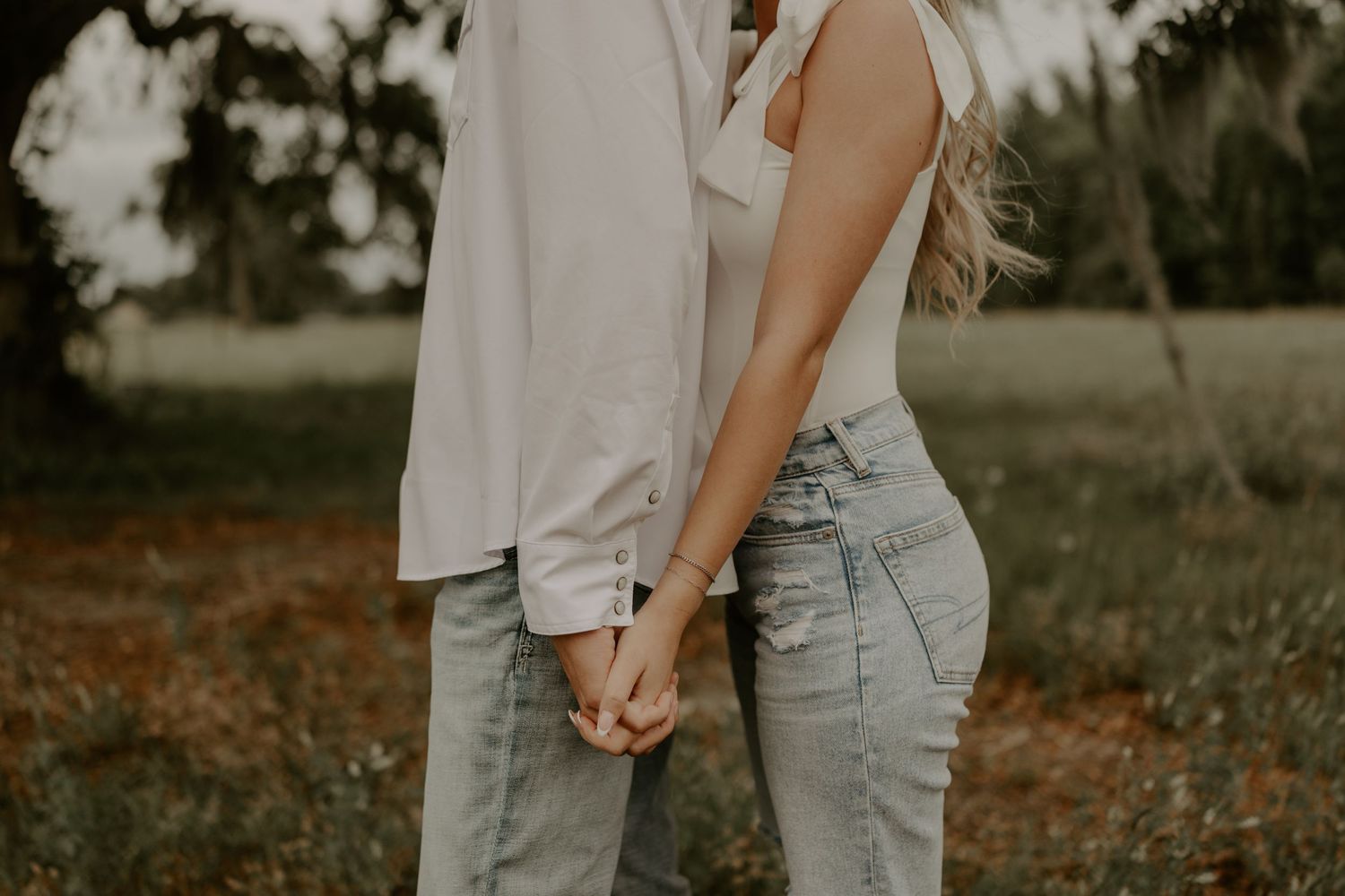 A romantic couple holds hands in an intimate outdoor setting with golden afternoon light and soft focus.