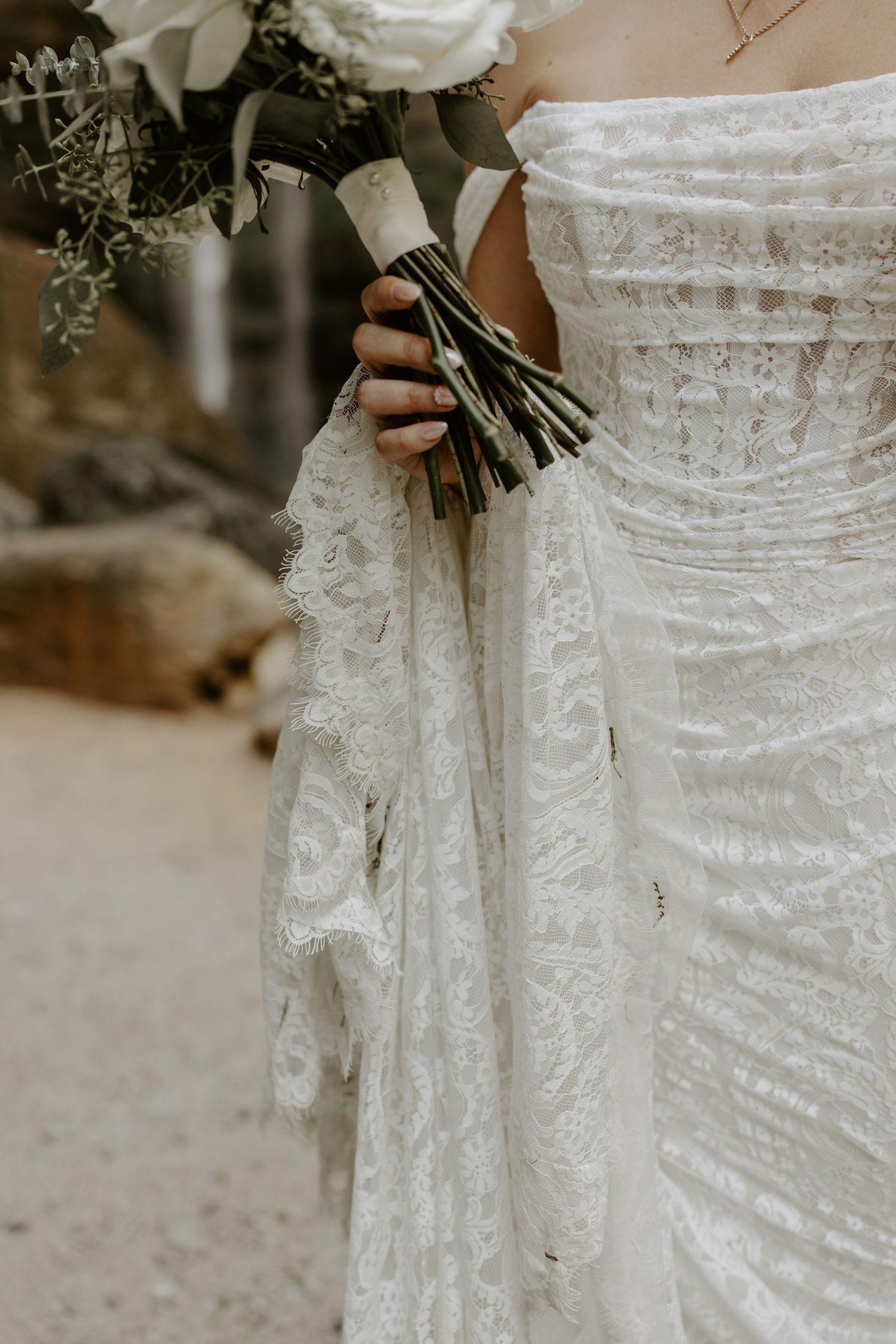 Close-up details of a white lace wedding dress with delicate embroidery patterns trailing down the skirt.