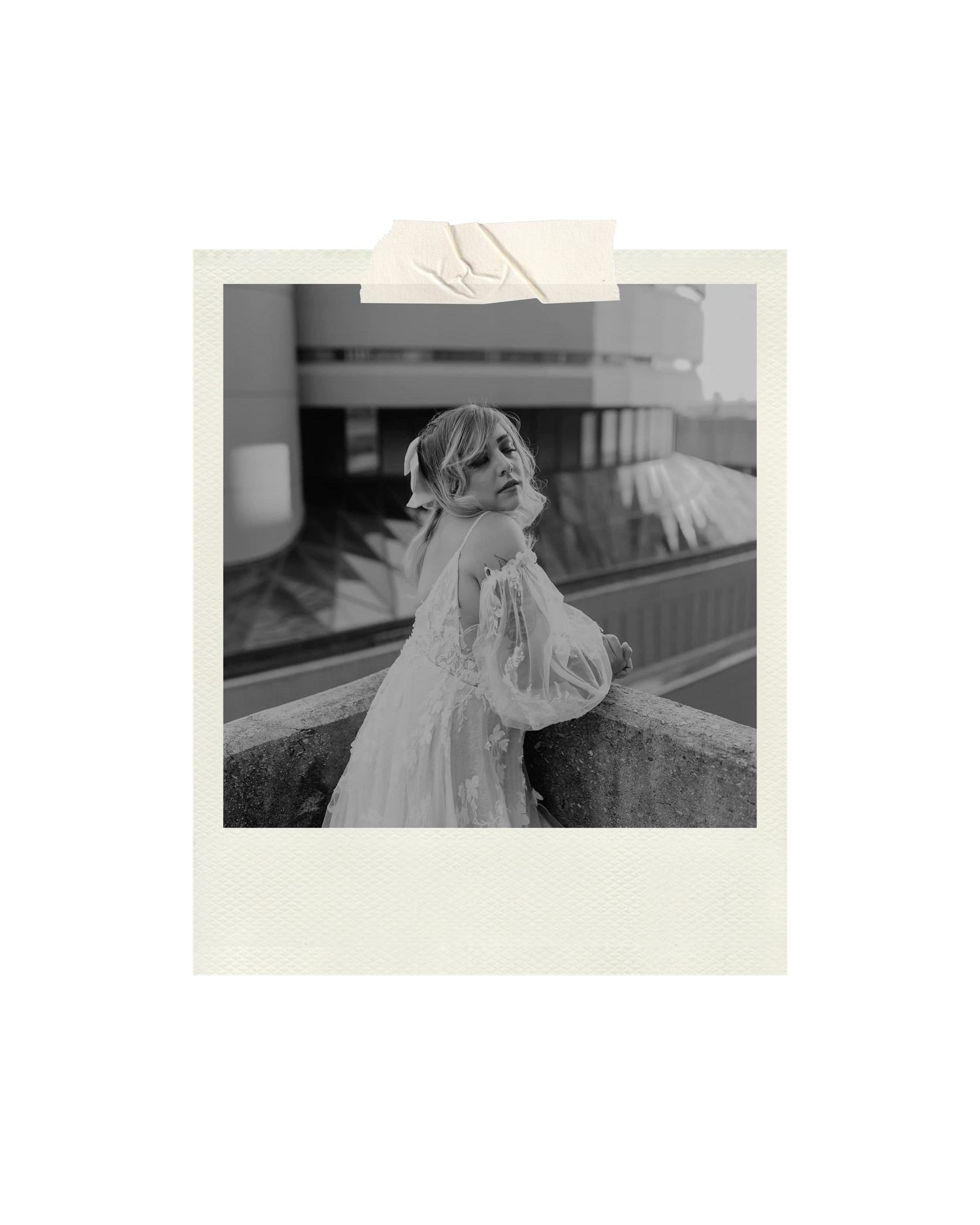 Black and white polaroid photo of a woman in a flowing white dress leaning on a ledge outdoors.