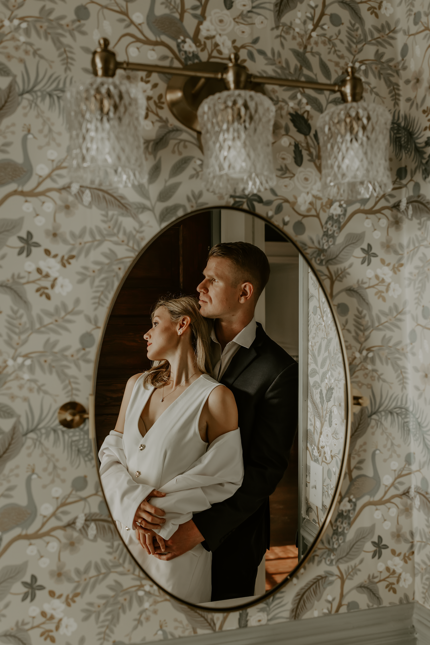 Romantic couple's reflection in bathroom mirror with ornate wallpaper and vintage lighting fixtures.

Georgia-based wedding and elopement ph