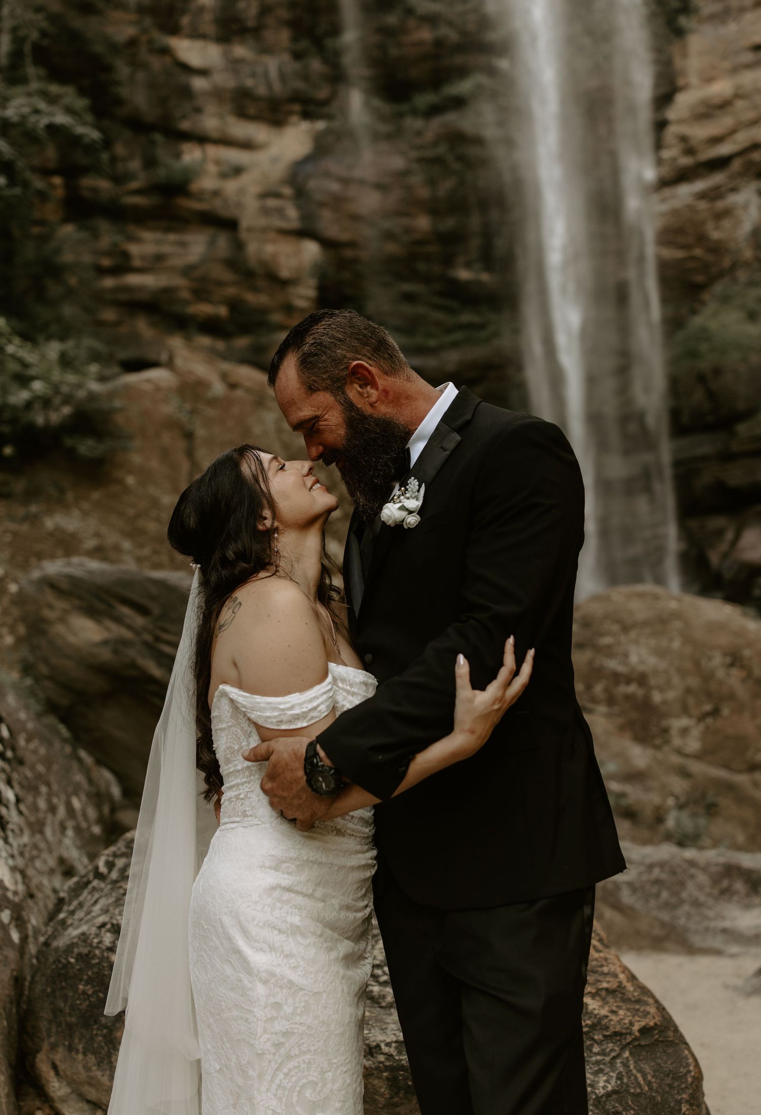 A newlywed couple shares a romantic kiss in front of a majestic waterfall backdrop, creating an intimate moment.