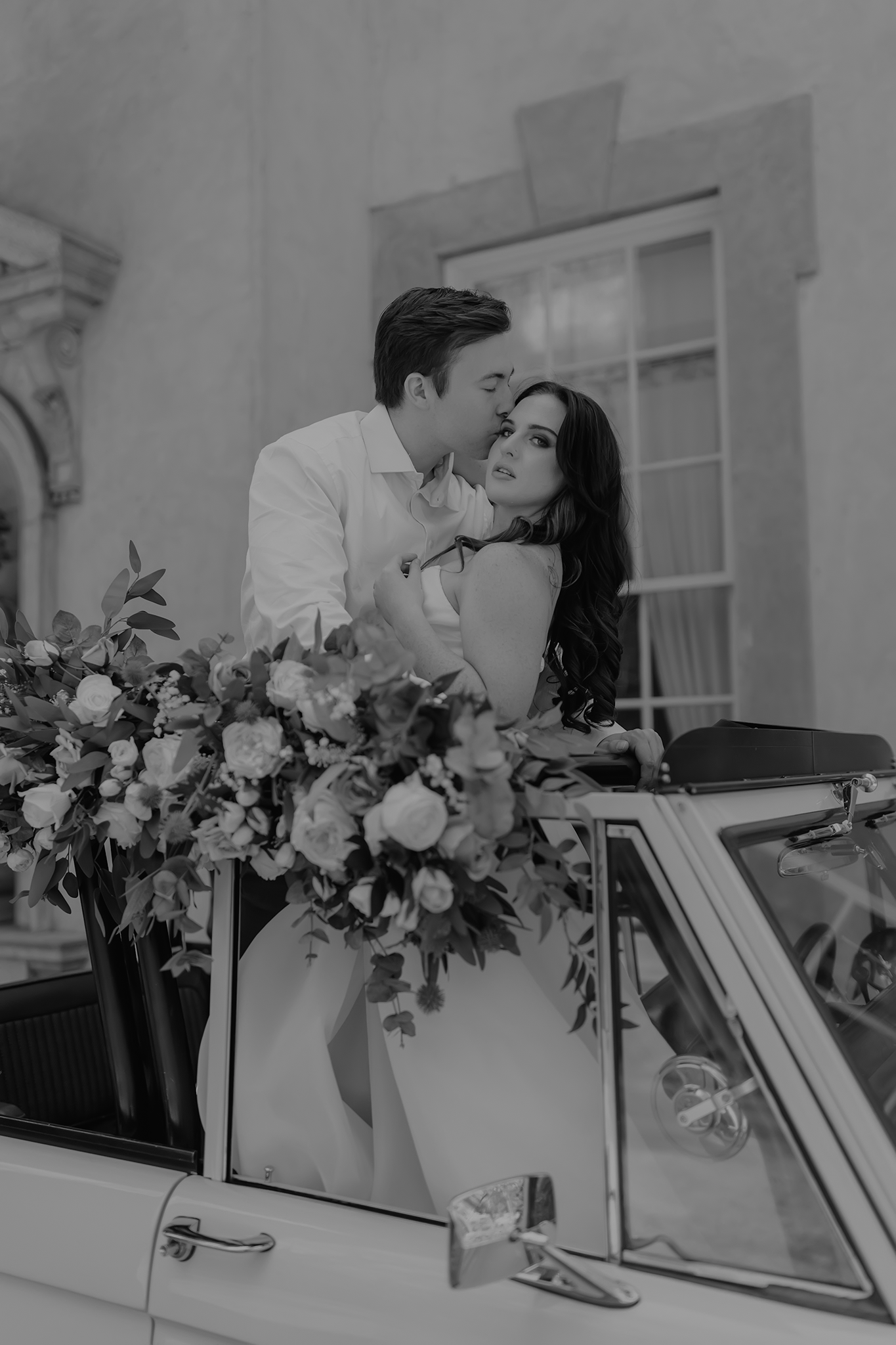 A romantic black and white photo series showing a couple sharing tender moments in a vintage car with floral decorations.