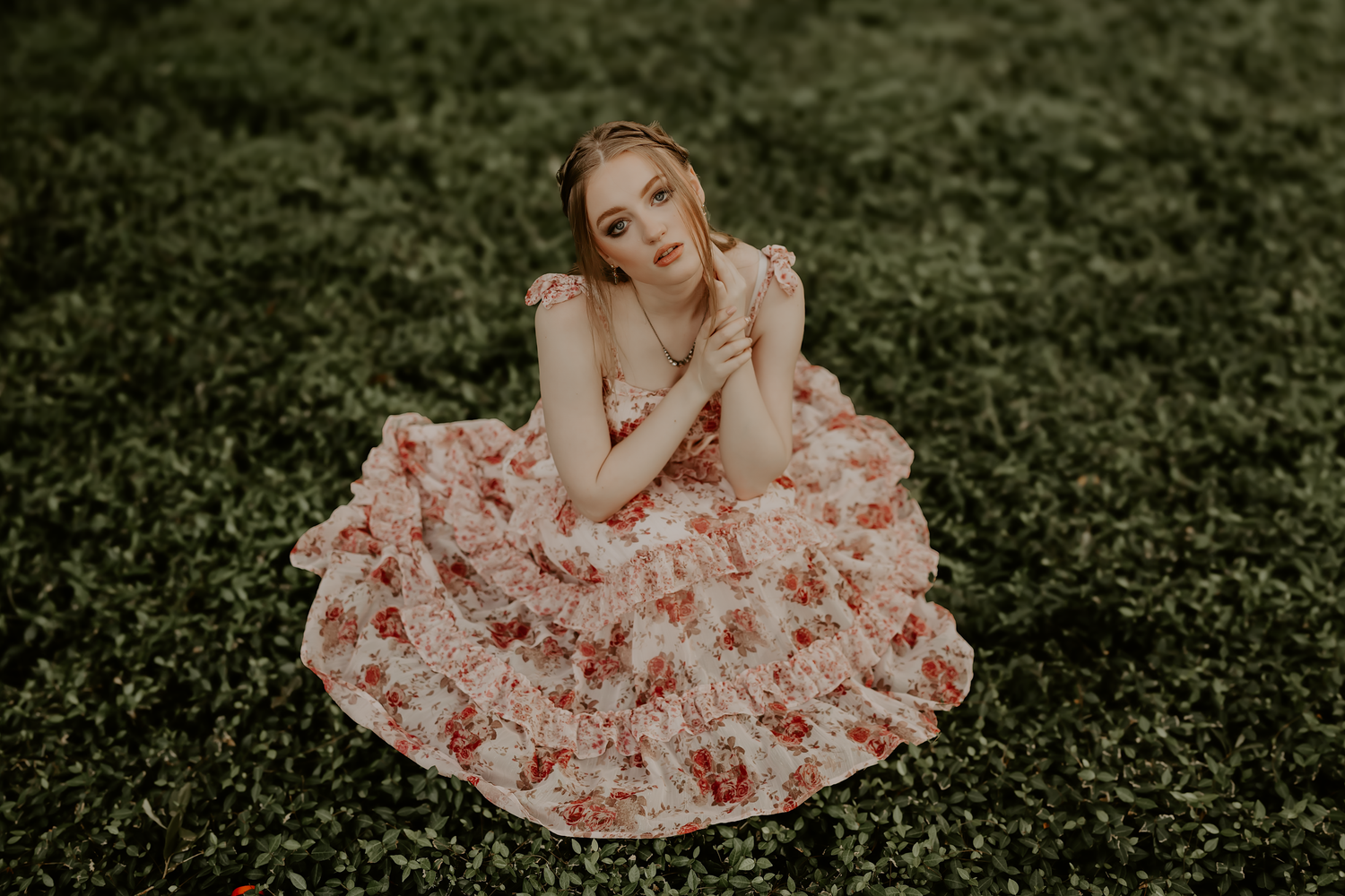 Woman in a floral printed pink dress twirls elegantly in a lush green garden setting.