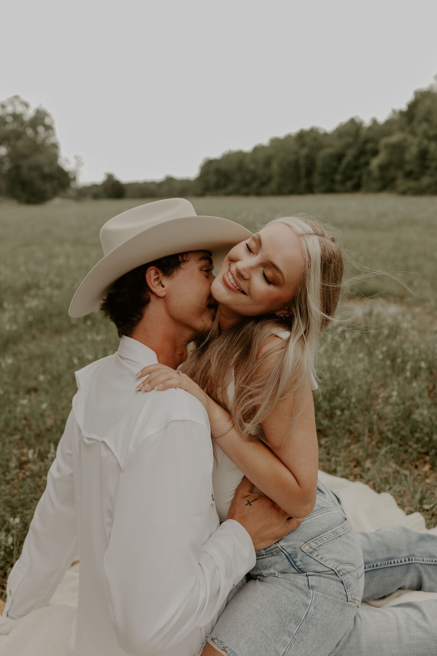 Romantic couple embraces in a sunny meadow wearing casual attire with cowboy hat and jeans.