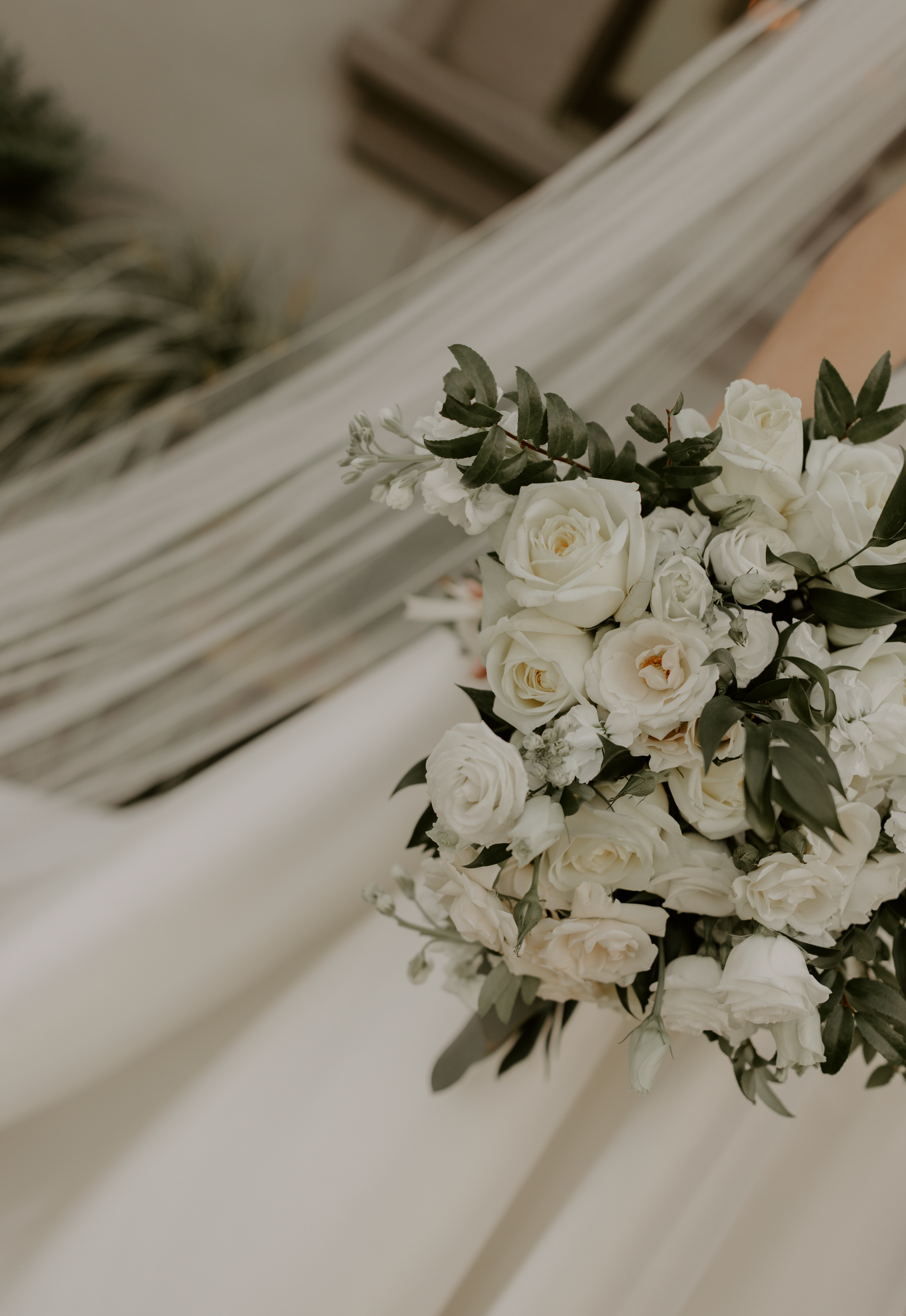 Elegant bridal bouquet of white roses and greenery against a flowing white wedding veil.