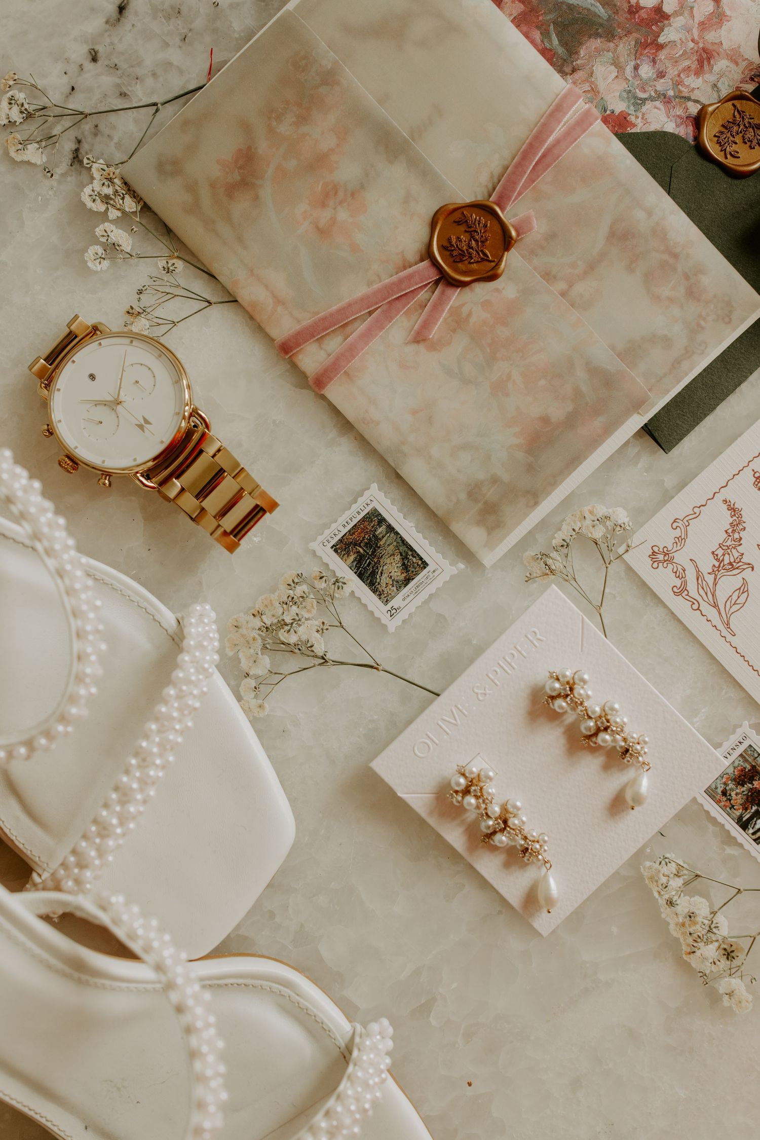 Flatlay of wedding accessories including watch, pearls, and sealed envelope.