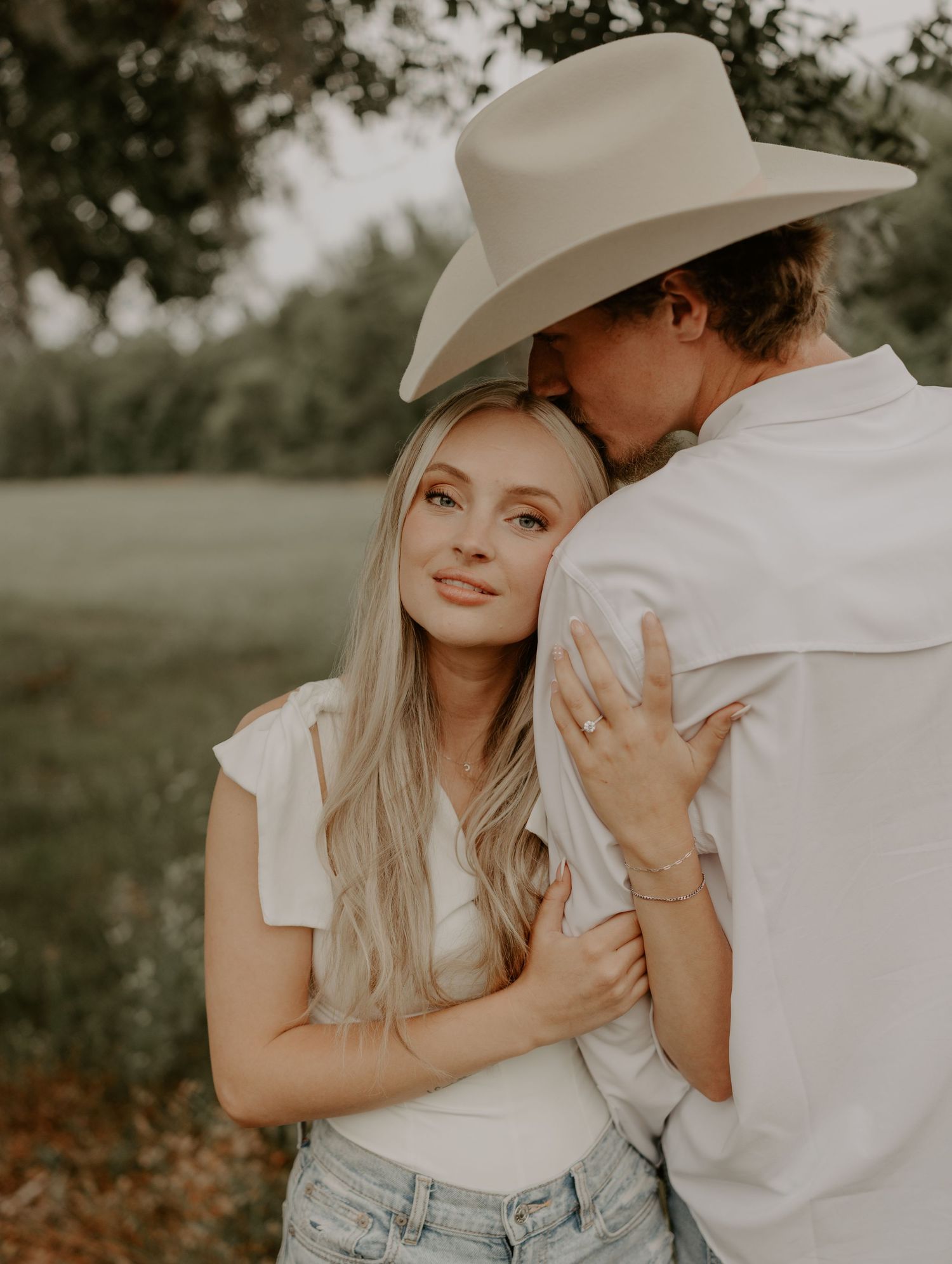 Romantic countryside portrait of couple embracing with man in cowboy hat.