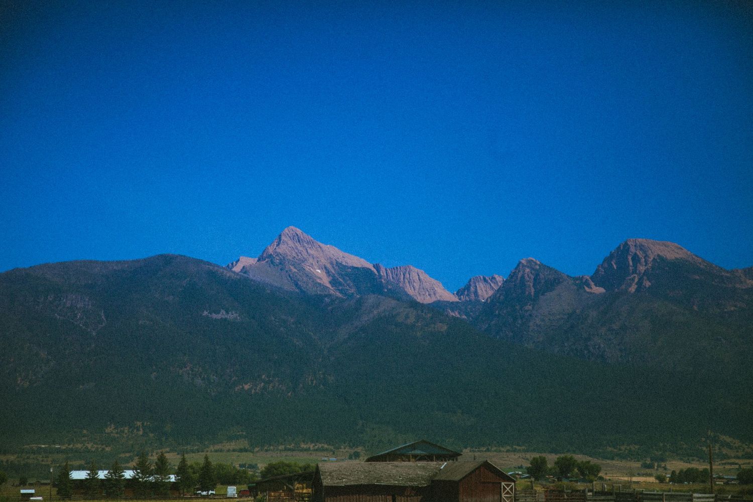 Mountain peaks rise against a deep blue sky in a scenic rural landscape.