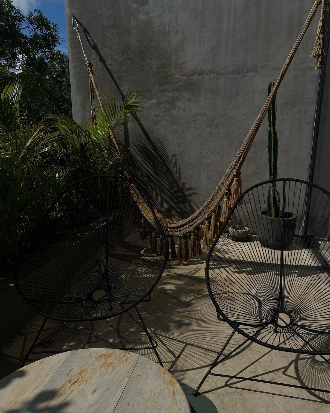 Modern outdoor patio setup with hammock and acapulco chairs casting dramatic shadows. Tulum, Mexico