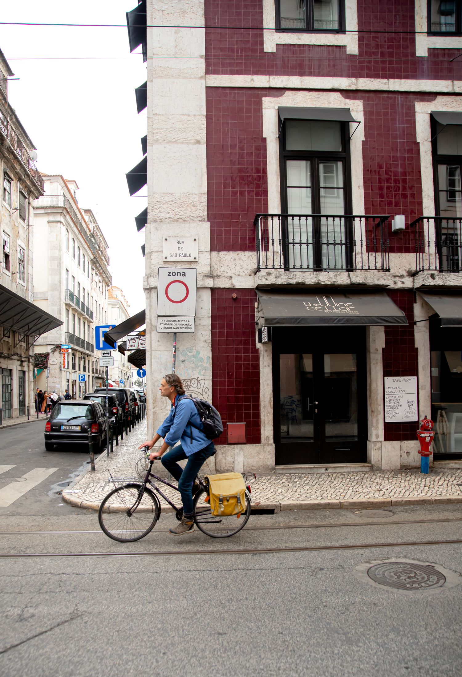 Person cycling past a burgundy and white building on a cobblestone street corner.