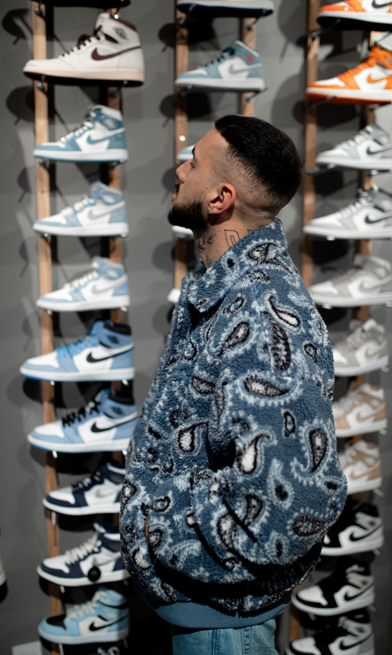 Person in paisley denim jacket admiring wall display of Nike sneakers.