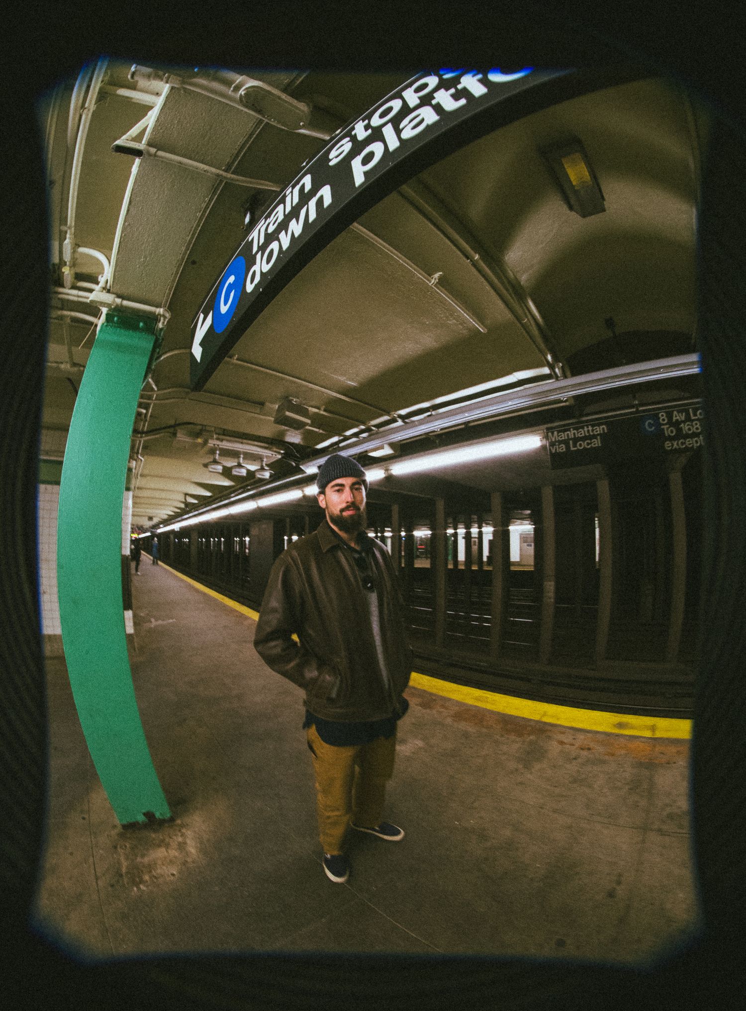 Fish-eye lens view of empty subway platform with green tiled pillars and curved architecture. New York.