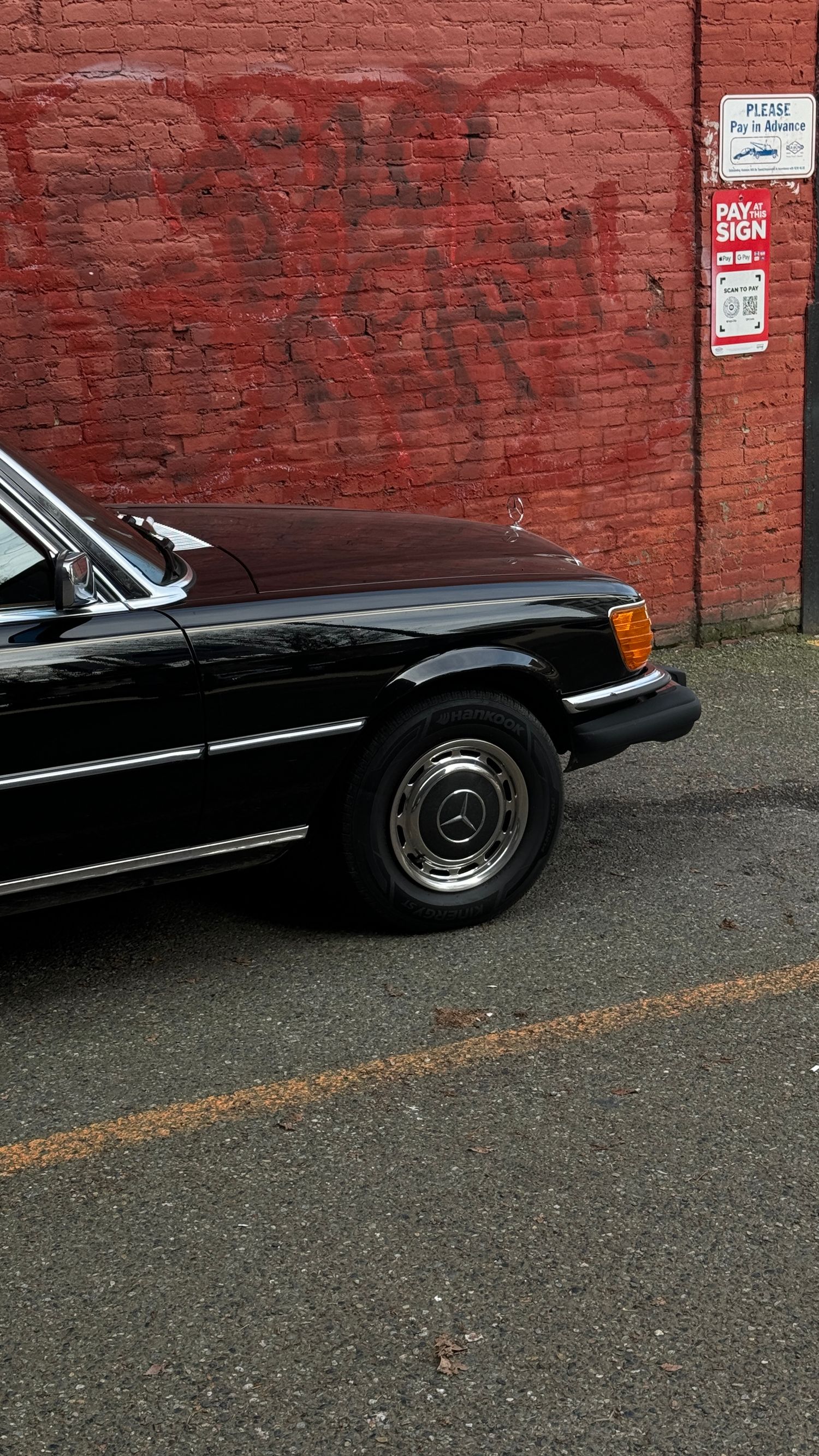 Front quarter view of classic black Mercedes-Benz against red brick wall.