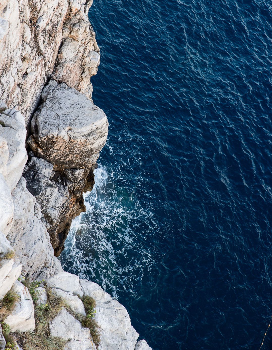 Dramatic white limestone cliff face meeting deep blue Mediterranean waters from aerial view.