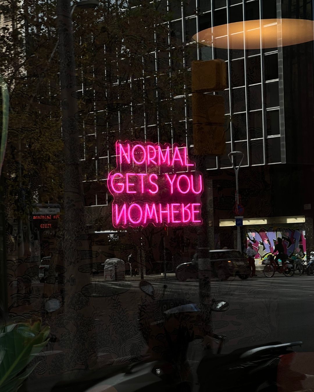 Pink neon sign reading 'Normal Gets You Nowhere' illuminated at night. Barcelona, Spain.