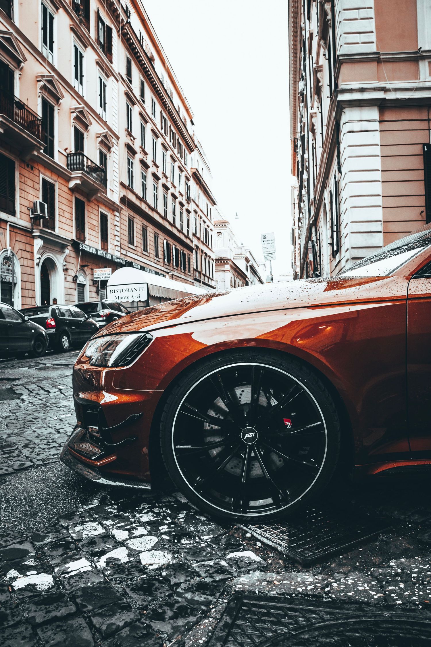 Orange luxury sports car wheel and fender detail on cobblestone street. Rome, Italy