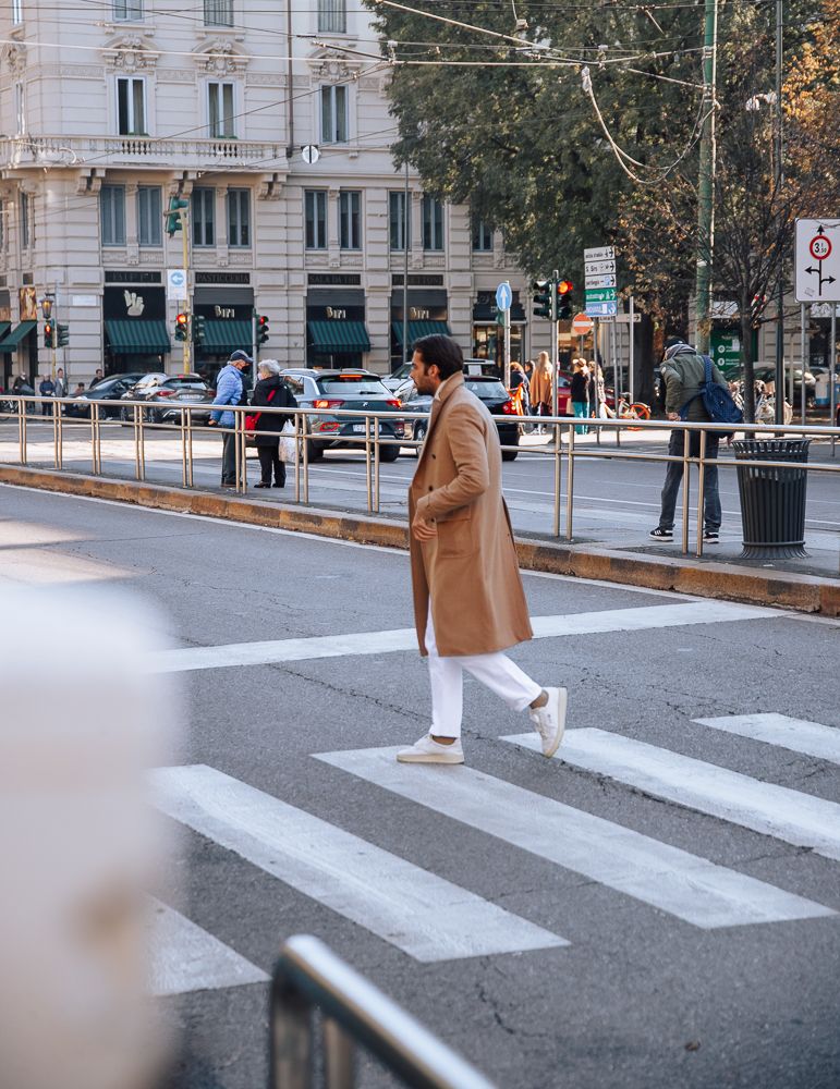 Person in a tan coat crossing a city street on a zebra crossing.