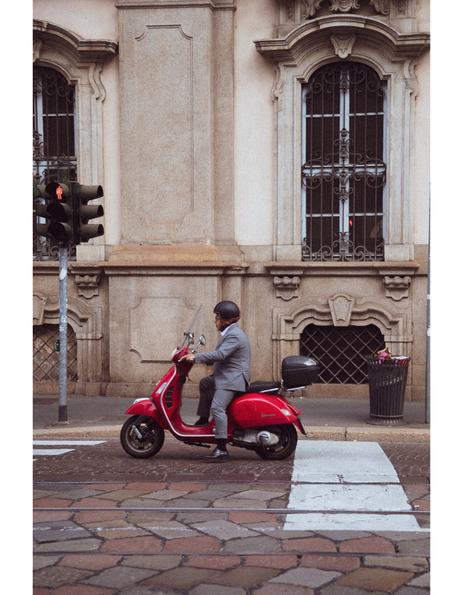 A red Vespa scooter parked in front of a classical building with ornate windows.