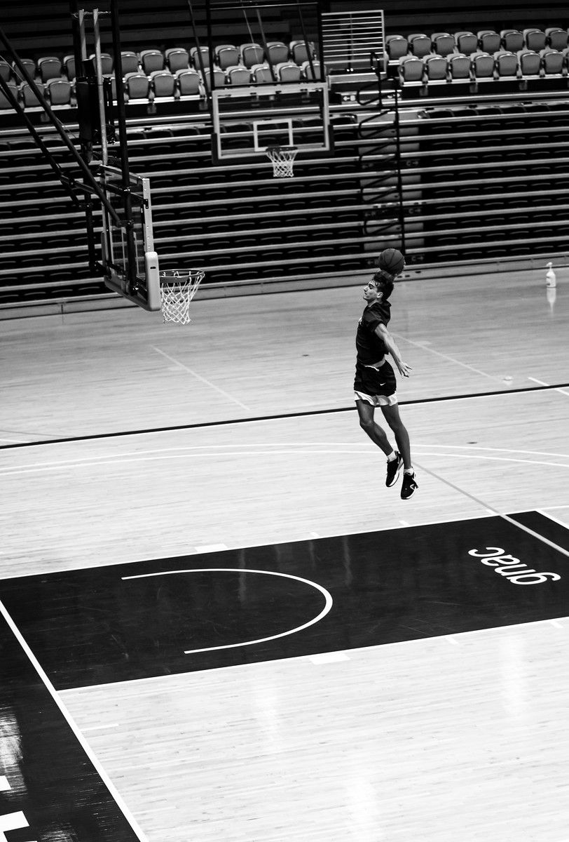 A basketball player soars for a dunk alone in an empty gymnasium. Black and white.