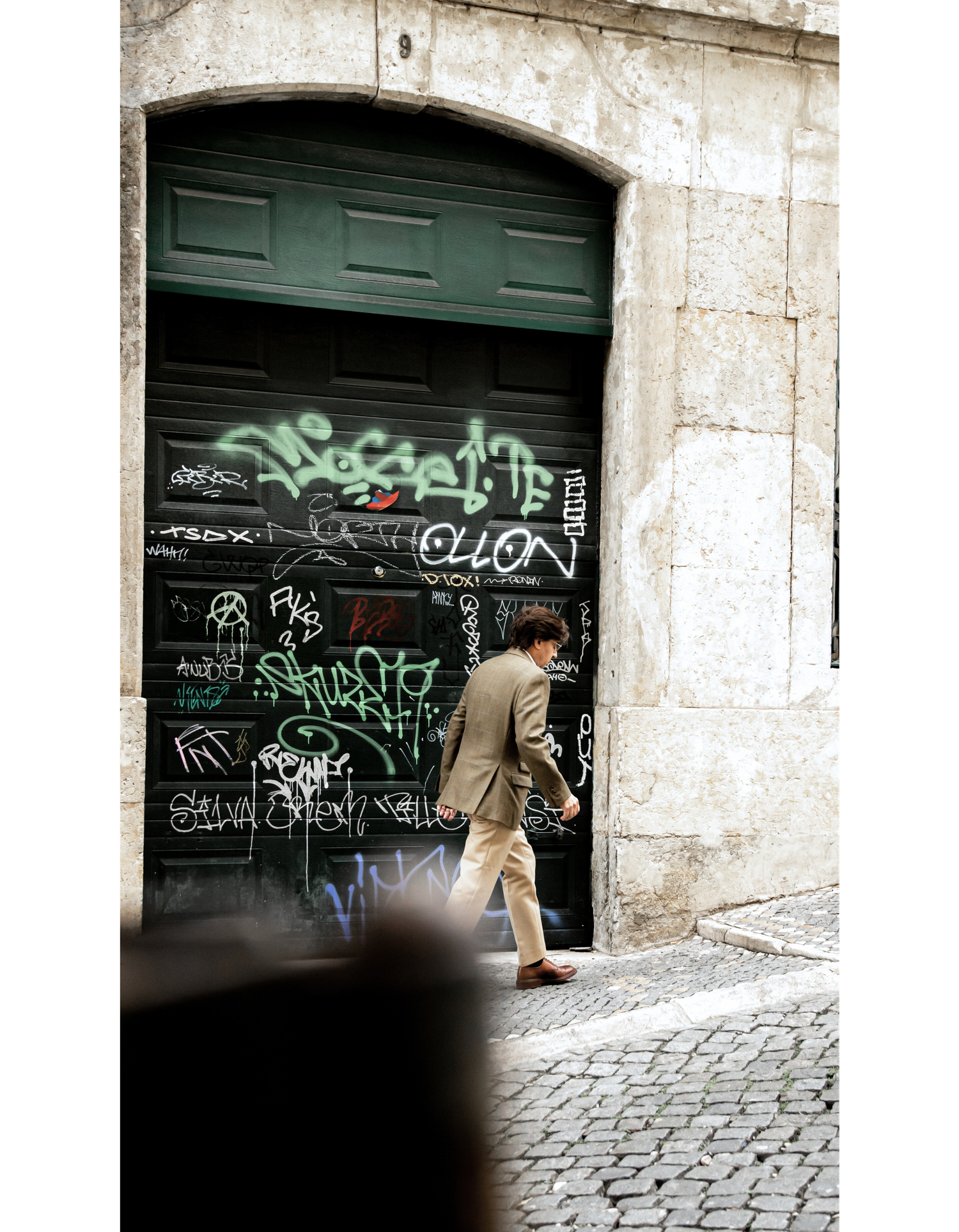 A graffiti-covered green door on an old stone building with cobblestone street.