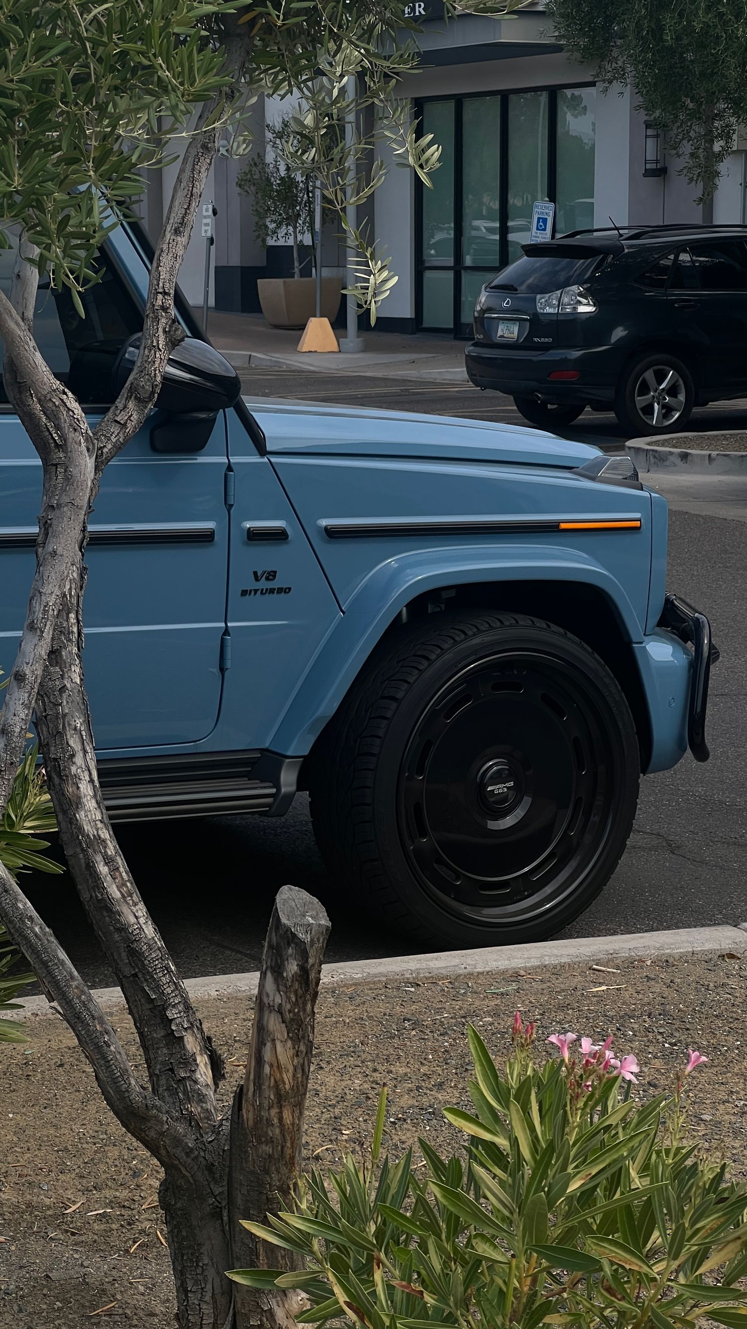 Light blue vintage Mercedes G-Wagon photographed with desert landscaping and modern building entrance.