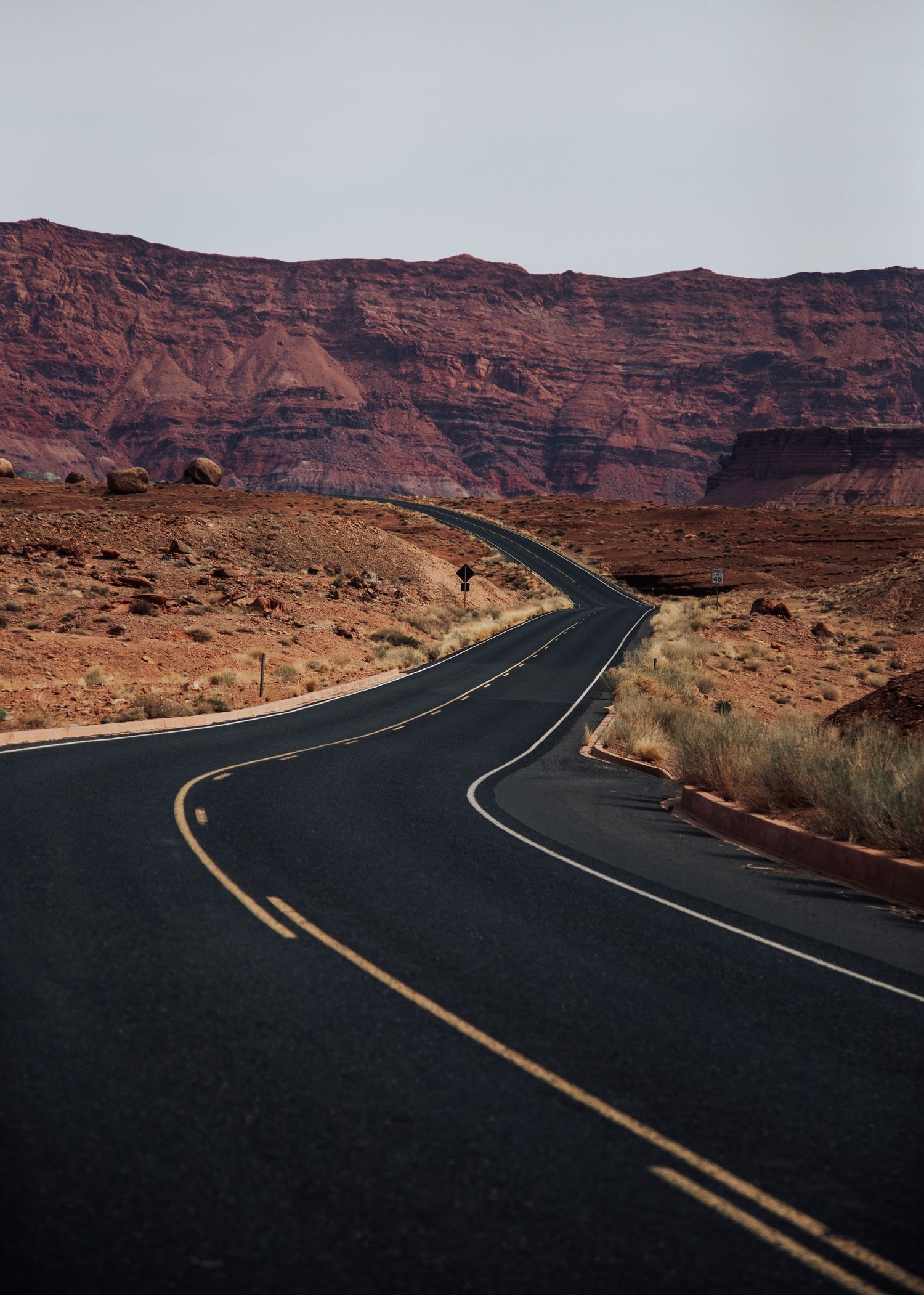 A winding desert highway curves through red rock formations in the American Southwest.