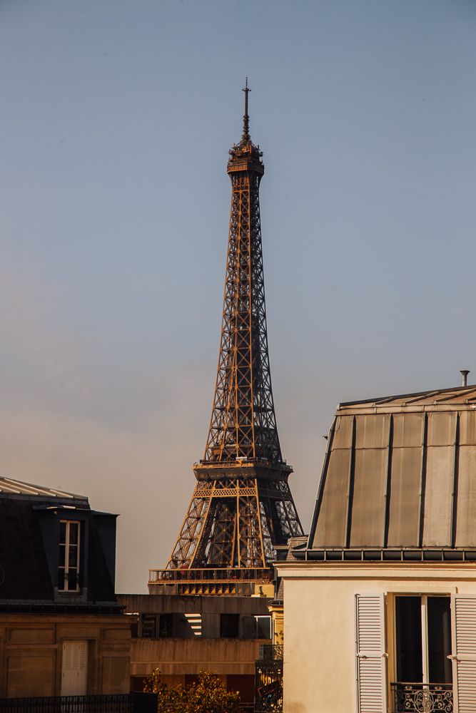 Eiffel Tower rises above Parisian rooftops against a clear sky at sunset.