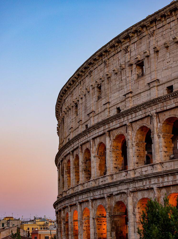 Ancient Roman Colosseum exterior illuminated at sunset with pink and orange sky in Rome, Italy.